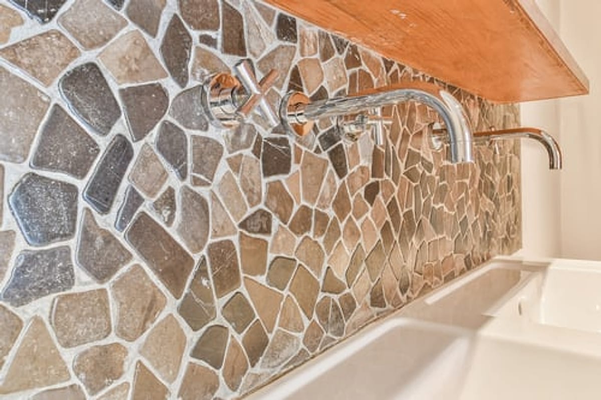 Natural stone mosaic backsplash installed behind a wall-mounted faucet in an Oklahoma City kitchen