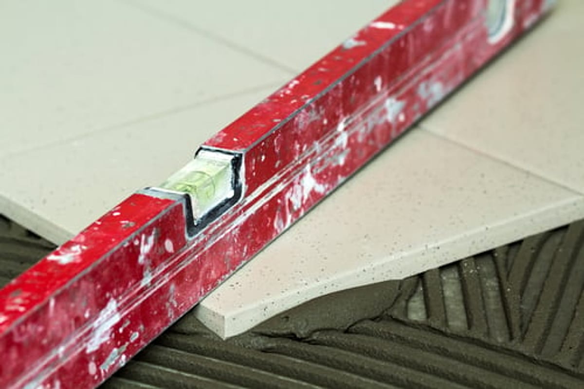Porcelain floor tile being set over notched thinset mortar and checked with a level during a bathroom installation