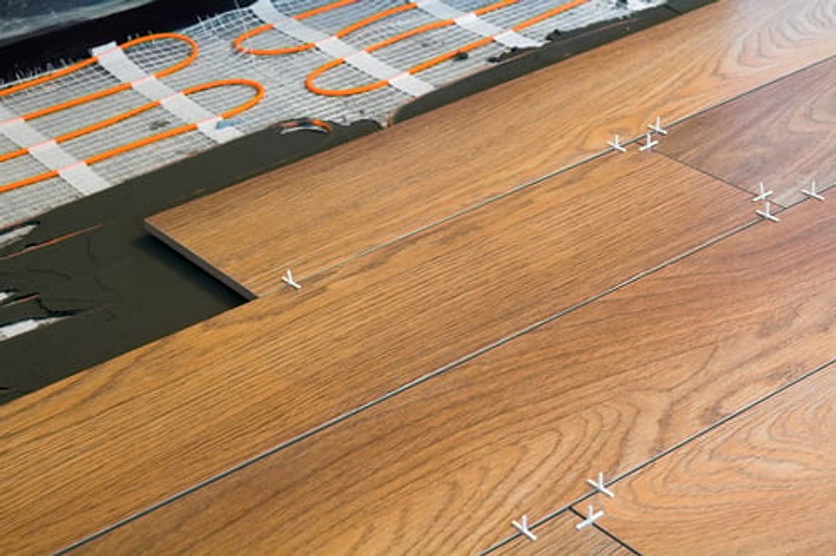 Wood-look plank flooring being installed over a prepared subfloor with tile spacers in place