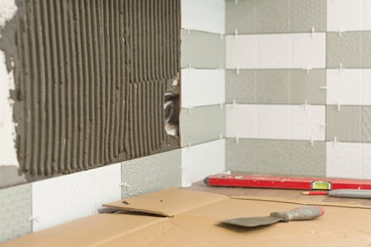 Ceramic wall tile being installed over notched thinset mortar with spacers and a level in an OKC bathroom