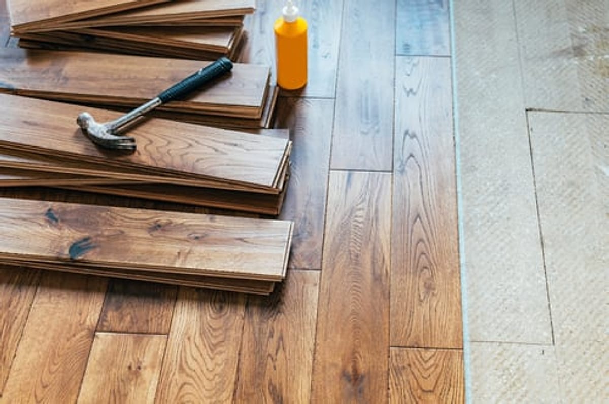 Stacked laminate flooring planks and a hammer laid out on a prepared subfloor in an Oklahoma City home